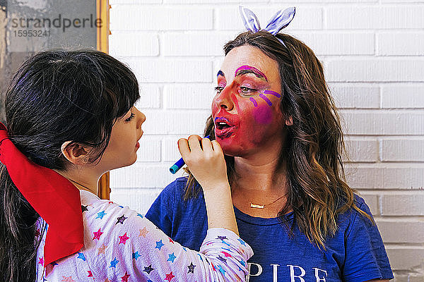 Tochter malt farbiges Make-up auf das Gesicht der Mutter