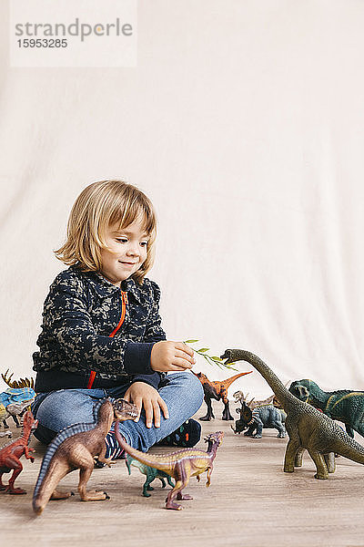 Porträt eines niedlichen kleinen Mädchens  das auf dem Boden sitzt und Spielzeug-Dinosaurier füttert