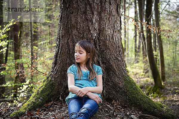 Bildnis eines Mädchens mit geschlossenen Augen  das sich im Wald an einen Baumstamm lehnt