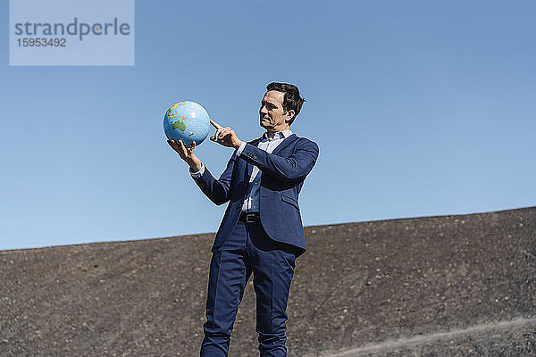 Ein reifer Geschäftsmann hält einen Globus auf einer stillgelegten Minendeponie