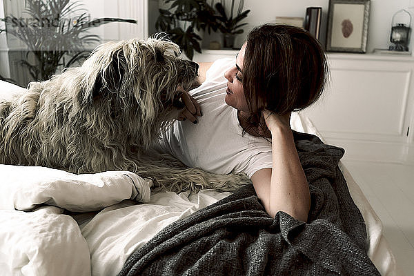 Reife Frau liegt auf dem Bett und spielt mit ihrem Hund