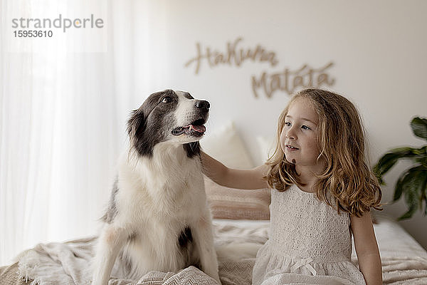 Porträt eines kleinen Mädchens  das mit seinem Hund auf dem Bett sitzt