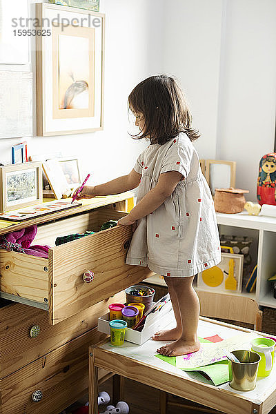 Mädchen zeichnet in voller Länge am Schrank  während sie im Haus auf dem Tisch steht