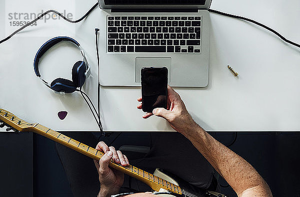 Draufsicht auf einen Mann  der mit Laptop und Smartphone online E-Gitarre lernt