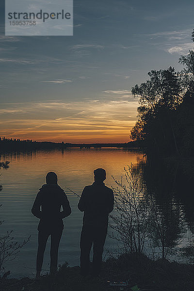 Paar steht am See  angelt im See bei Sonnenuntergang