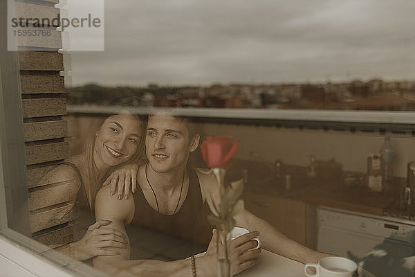 Romantisches junges Paar mit roter Rose hinter Fensterscheibe