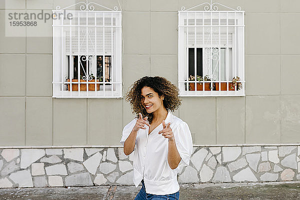 Porträt einer jungen Frau  die ein weißes Hemd trägt und mit den Fingern zeigt