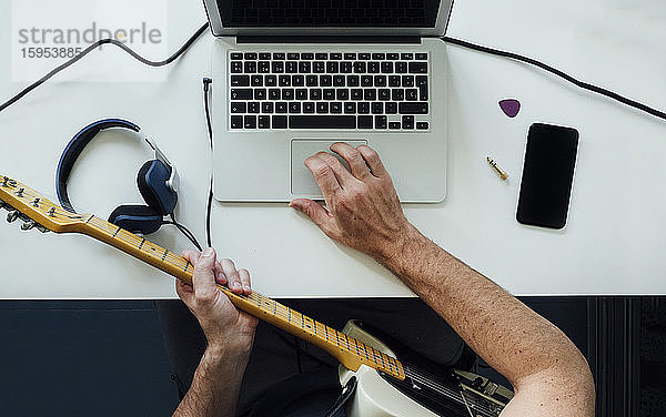 Draufsicht auf einen Mann  der mit einem Laptop online E-Gitarre lernt