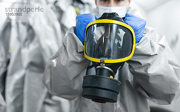 Nahaufnahme eines Sanitärarbeiters mit Gasmaske beim Anziehen in der Umkleidekabine