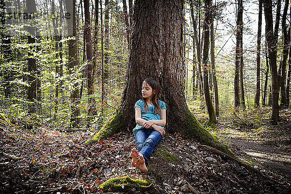 Mädchen mit geschlossenen Augen an Baumstamm gelehnt im Wald