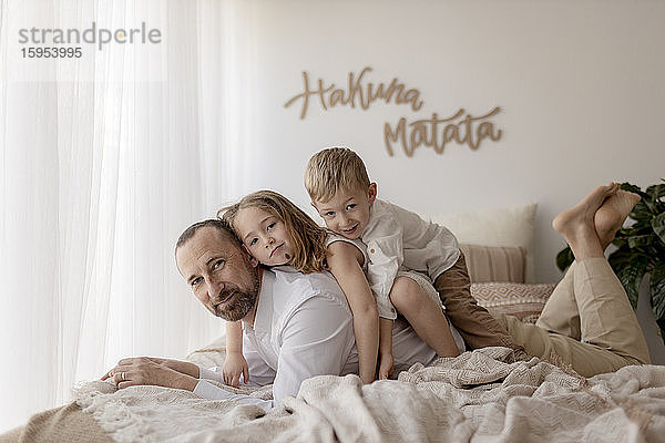 Familienporträt des Vaters und seiner beiden Kinder  die zusammen mit dem Hund auf dem Bett liegen