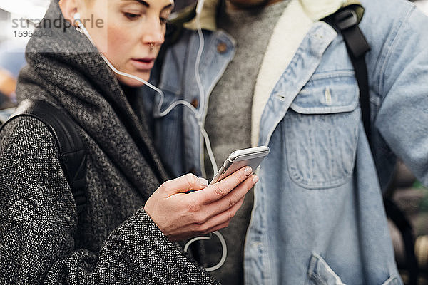 Junges Paar mit Ohrstöpseln mit Smartphone in der U-Bahn