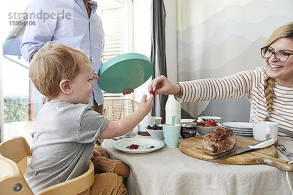 Kleiner Junge nimmt von seiner Mutter am Frühstückstisch Himbeeren