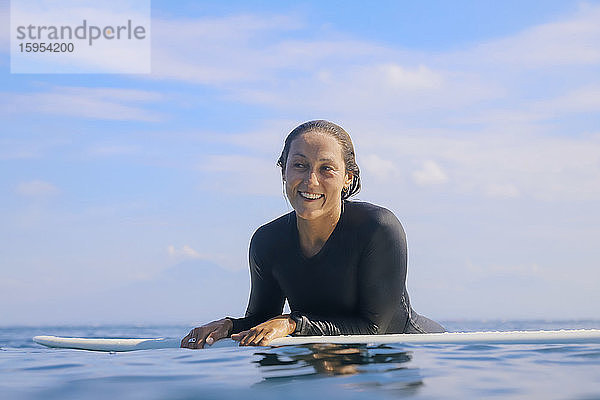 Porträt einer glücklichen Frau  die auf einem Surfbrett im Meer liegt  Bali  Indonesien