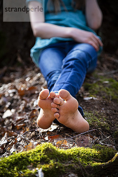 Schnittansicht eines barfuss auf dem Boden sitzenden Mädchens im Wald