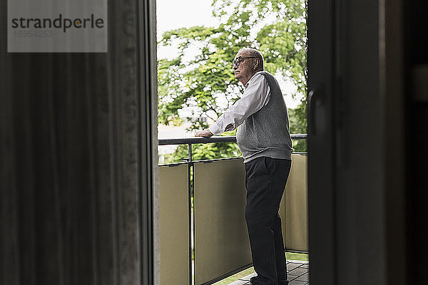 Älterer Mann steht auf Balkon und schaut in die Ferne