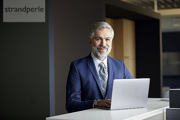 Portrait eines reifen Geschäftsmannes mit Laptop im Büro