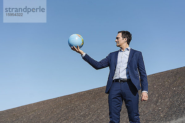 Ein reifer Geschäftsmann hält einen Globus auf einer stillgelegten Minendeponie