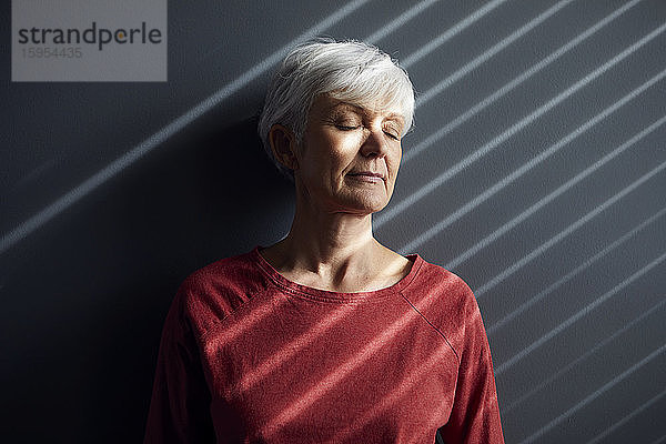 Porträt einer älteren Frau mit geschlossenen Augen an der Wand lehnend