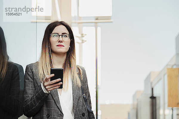 Porträt einer jungen Geschäftsfrau mit Smartphone beim Blick aus der Ferne