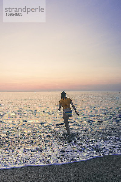 Rückansicht einer Teenagerin  die bei Sonnenaufgang am Strand an der Küste entlang läuft