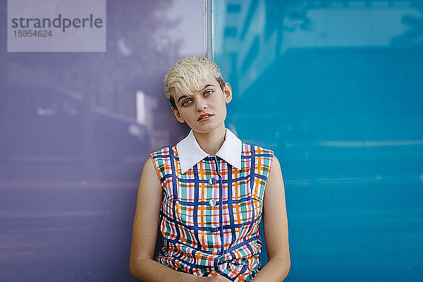 Porträt eines weiblichen Teenagers in farbigem Kleid  der sich an eine mehrfarbige Glaswand lehnt