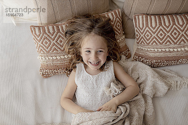 Porträt eines lachenden  auf dem Bett liegenden kleinen Mädchens