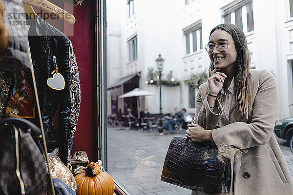 Lächelnde mittelgroße erwachsene Frau betrachtet Schaufensterauslage eines Geschäfts in der Stadt