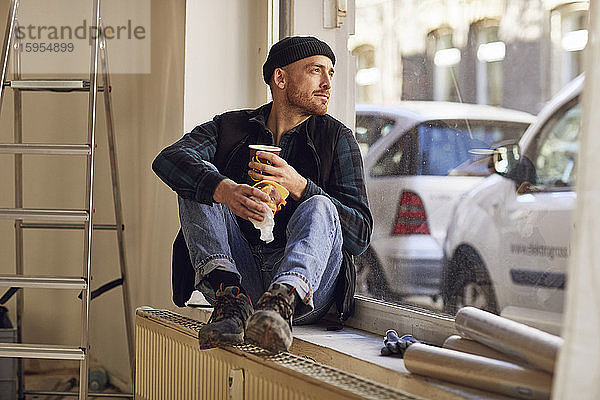 Mann renoviert Ladenstandort  sitzt auf der Fensterbank  trinkt Kaffee