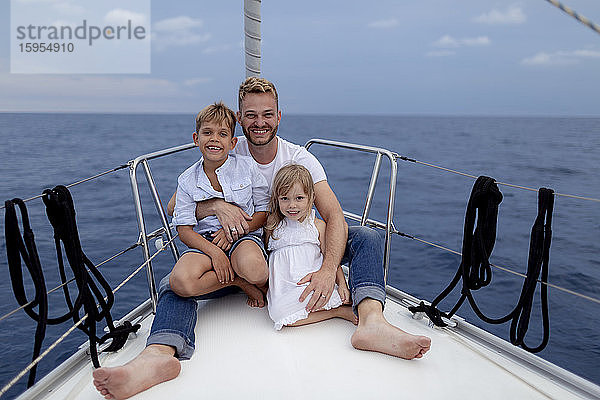 Vater mit seinen Kindern während der Segelfahrt auf dem Bootsdeck sitzend