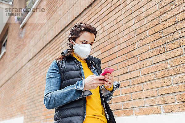 Frau  die ihr Gesicht mit einer Schutzmaske bedeckt und ein Smartphone benutzt