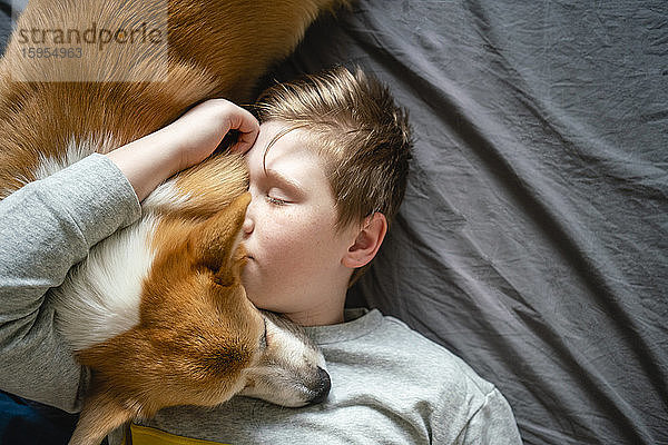 Porträt eines Jungen  der auf dem Bett liegt und seinen Hund kuschelt