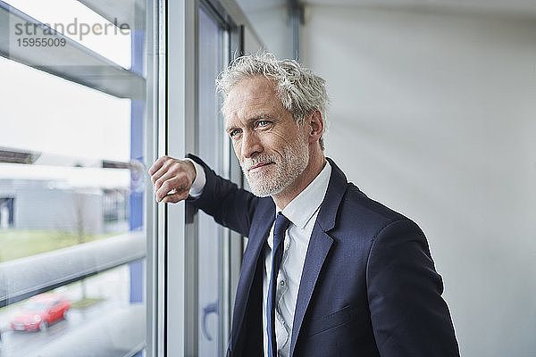 Porträt eines selbstbewussten Geschäftsmannes  der aus dem Fenster schaut