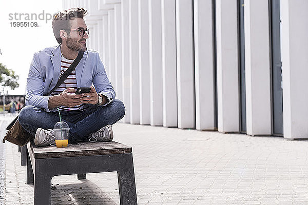 Junger Mann in der Stadt sitzt auf einer Bank mit Handy  Lissabon  Portugal