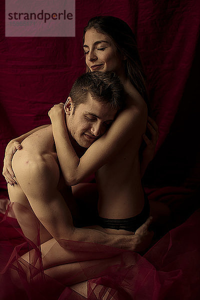 Intimes junges Paar umarmt sich vor einem Rubinvorhang