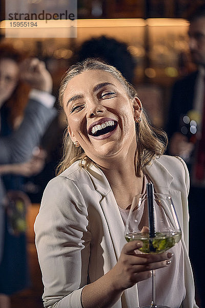 Porträt einer glücklichen jungen Frau bei einem Cocktail in einer Bar