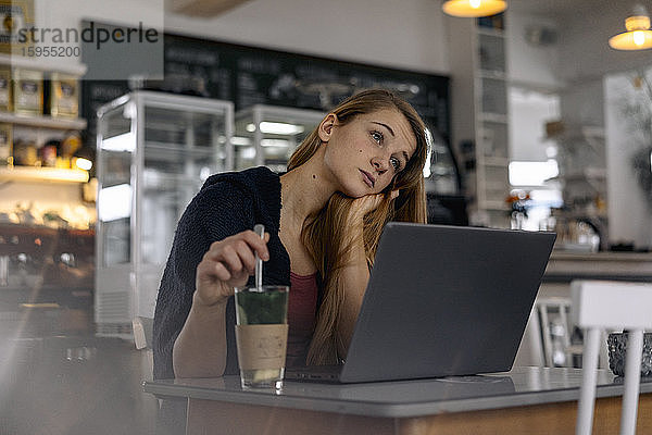Tagträumende junge Frau mit Laptop in einem Cafe