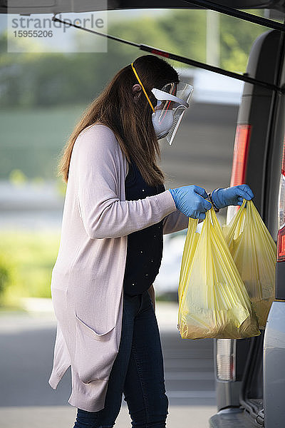 Seitenansicht eines Kunden  der auf dem Parkplatz eines Supermarktes Plastiktüten am Kofferraum eines Fahrzeugs hält