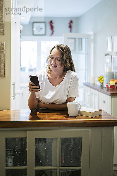 Junge Frau benutzt Smartphone in der Küche