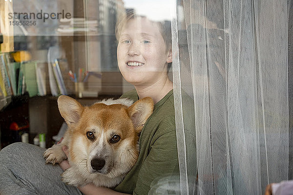 Porträt eines lächelnden Jungen und seines Hundes  die aus dem Fenster schauen