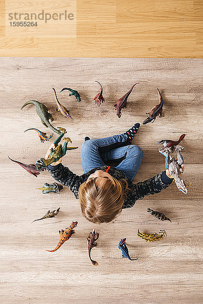 Kleines Mädchen sitzt auf dem Boden und spielt mit Spielzeug-Dinosauriern um sich herum  Draufsicht