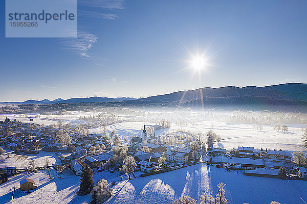 Deutschland  Bayern  Reichersbeuern  Drohnenblick auf die Sonne  die über das verschneite Dorf scheint