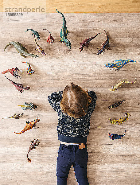Kleines Mädchen liegt auf dem Boden und spielt mit Spielzeug-Dinosauriern um sich herum  Draufsicht