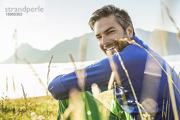 Porträt eines lächelnden Mannes  der in der Morgendämmerung auf einer Wiese in den Bergen sitzt  Achenkirch  Österreich