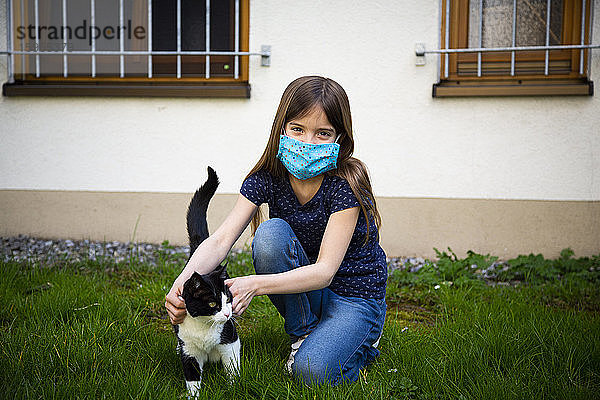Mädchen trägt Schutzmaske und streichelt ihre Katze im Garten