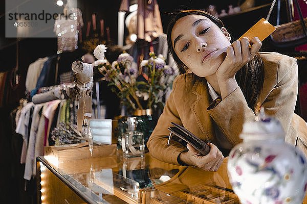 Neugierige Frau mit Kreditkarte und Brieftasche betrachtet Vase im Secondhand-Laden