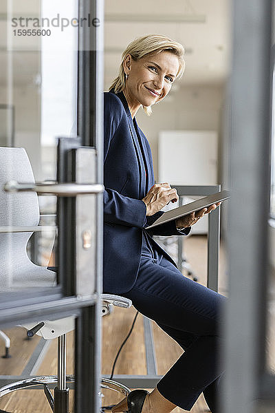 Porträt einer lächelnden blonden Geschäftsfrau mit Tablett im Konferenzraum