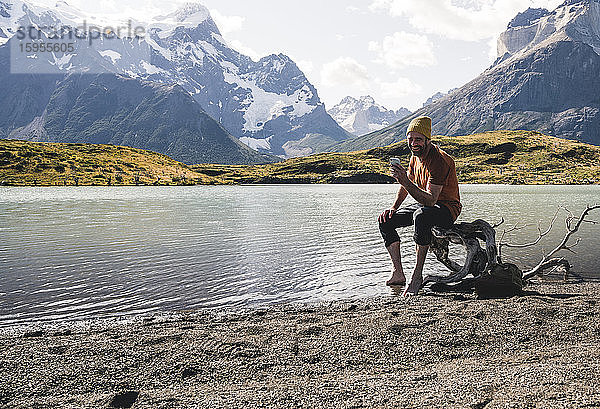 Mann benutzt Mobiltelefon in einer Berglandschaft am Seeufer im Torres del Paine Nationalpark  Patagonien  Chile