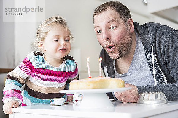 Vater und Tochter blasen Geburtstagskerzen aus