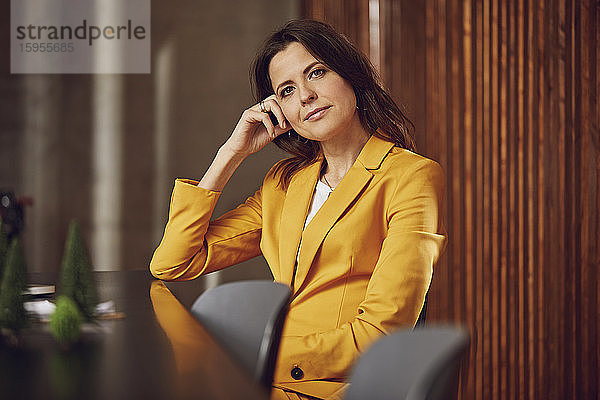 Porträt einer Geschäftsfrau im gelben Anzug am Schreibtisch im Büro sitzend